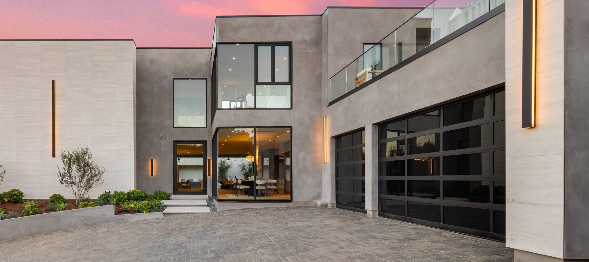 Black-framed glass garage doors across the lower floor of a modern stucco home at dusk