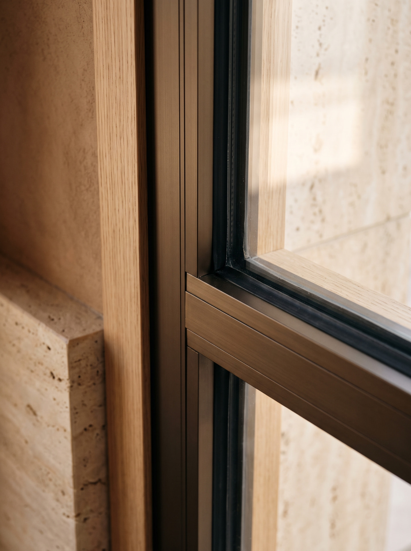 Close-up of a dark bronze window frame with oak trim set in travertine stone