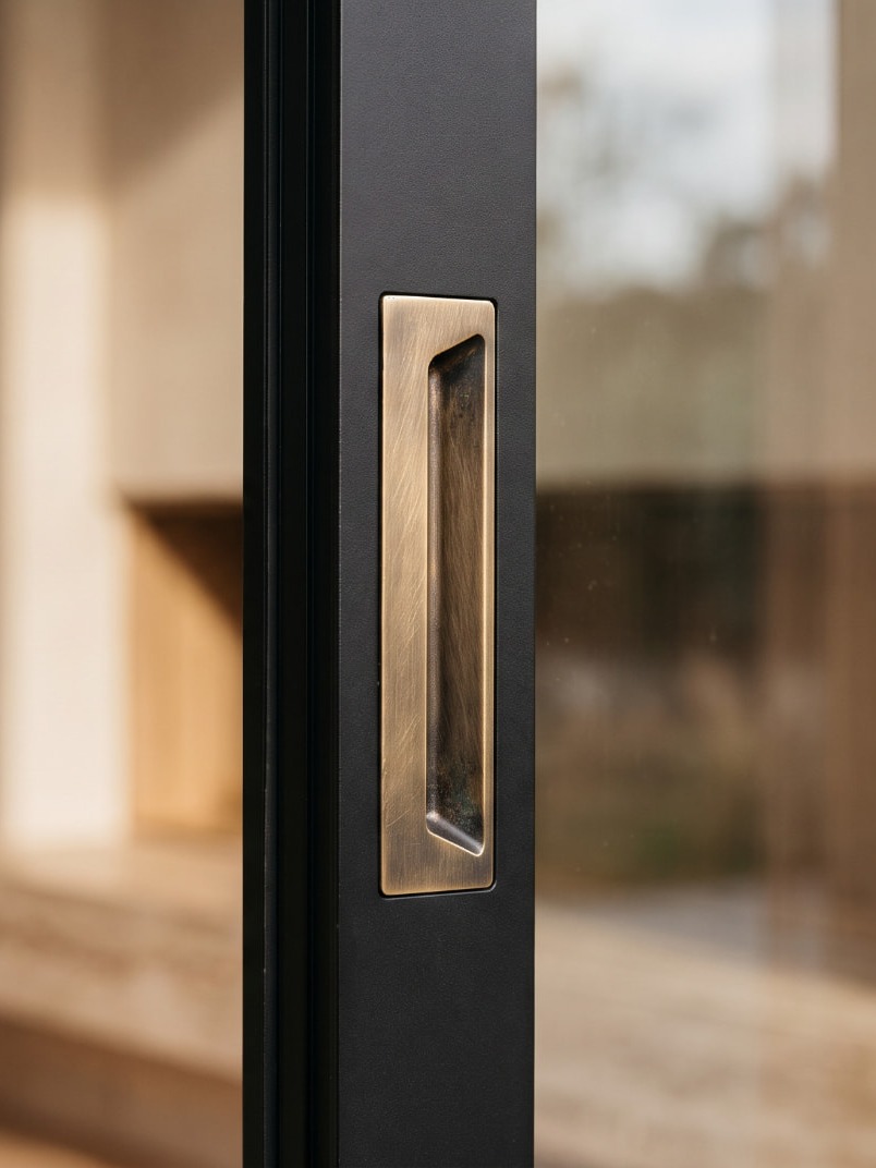 A brass pull sunk flush into the stile, there only when your hand finds it