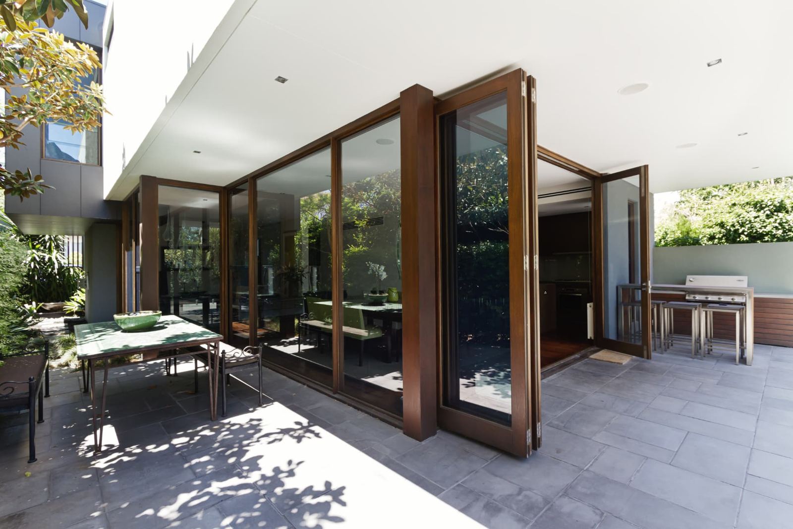 Timber-framed folding glass walls opened from a dining room onto a paved patio