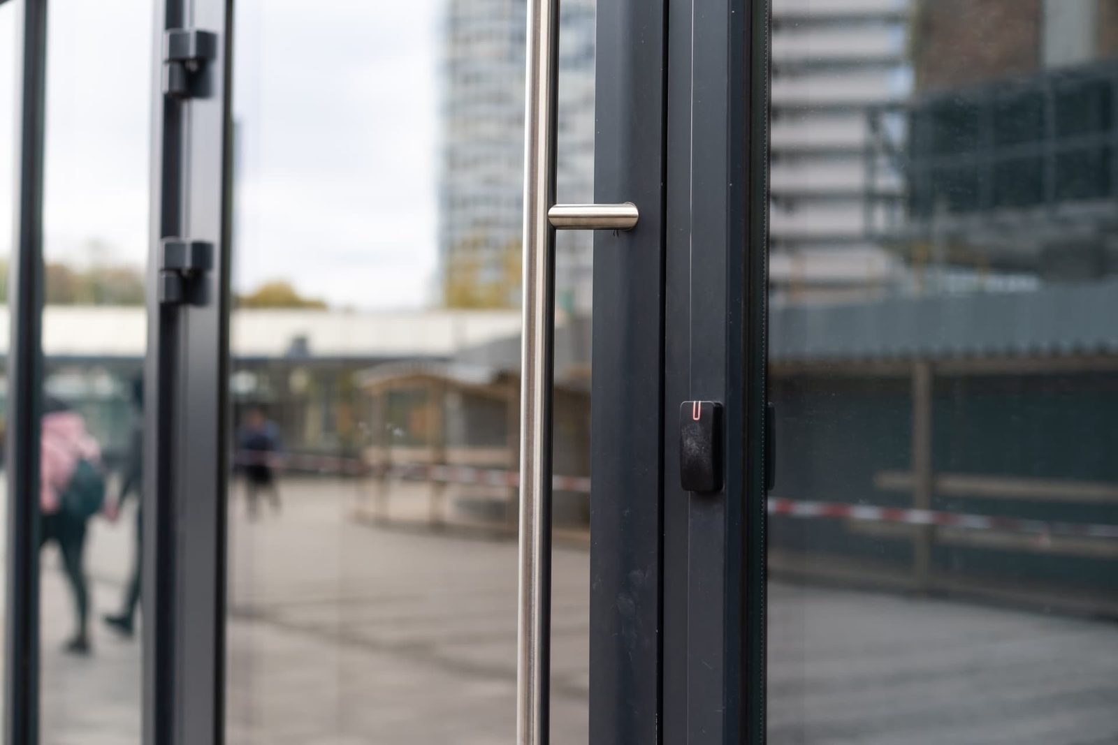 Brushed steel bar handle and keycard reader on a dark-framed commercial glass entrance