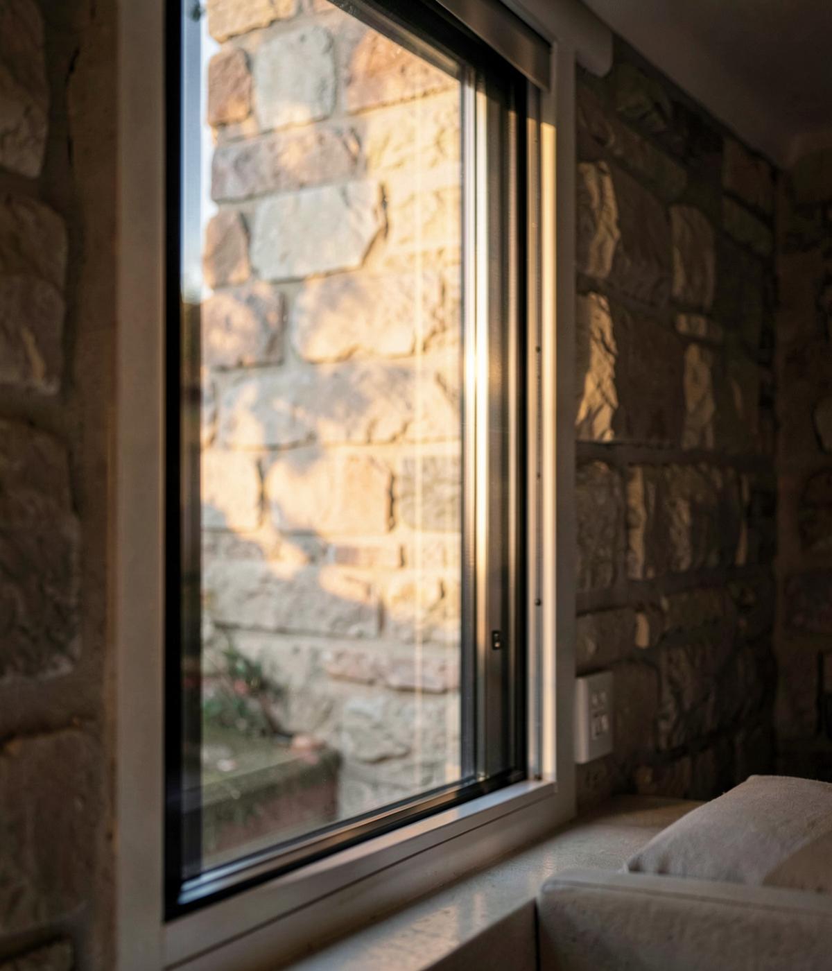 Slim-framed window against a stone wall in warm morning light